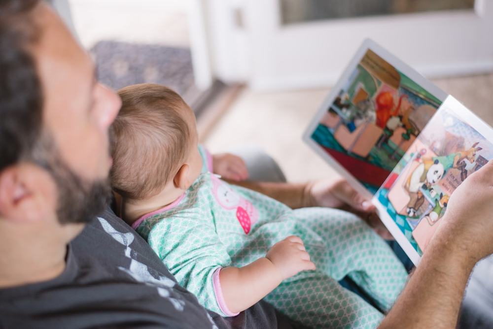 Adulto com um bebê no colo, lendo um livro juntos