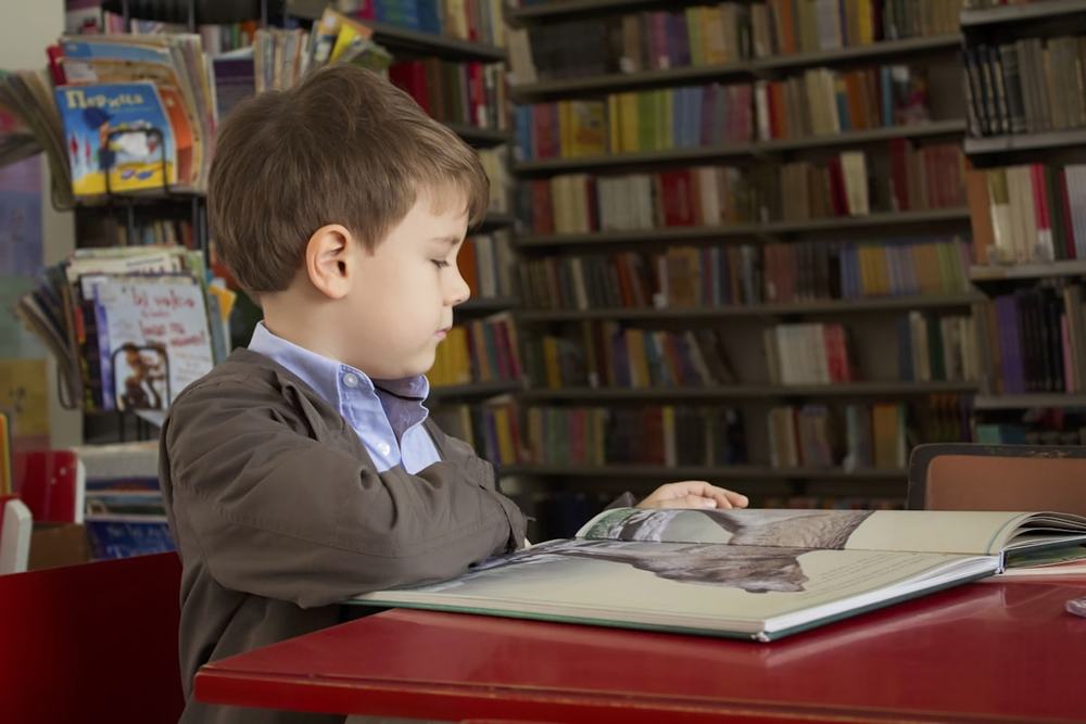 Menino sentado a uma mesa, lendo um livro
